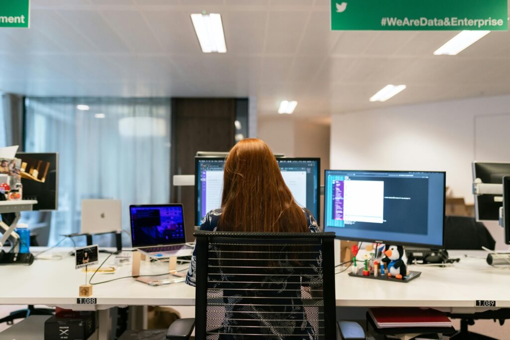 Back view of a female software engineer working at a multi-monitor setup in an office.